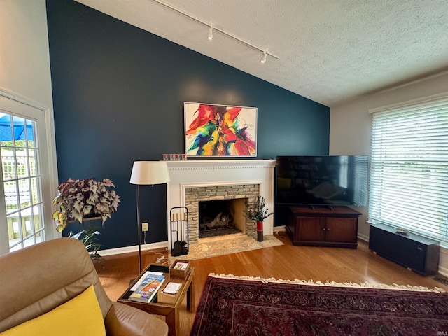 living room with vaulted ceiling, track lighting, wood finished floors, plenty of natural light, and a textured ceiling