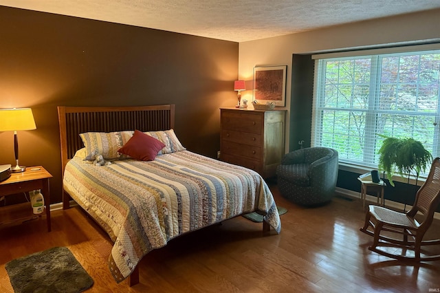bedroom with wood finished floors, multiple windows, a textured ceiling, and baseboards