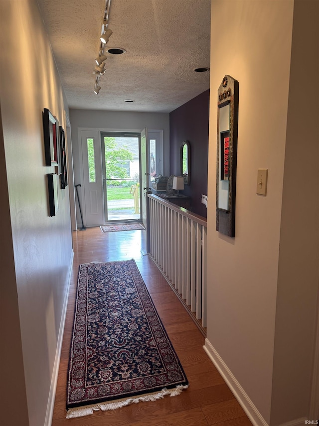 hallway featuring rail lighting, baseboards, wood finished floors, and a textured ceiling