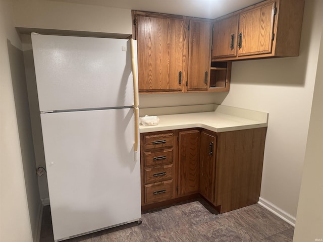 kitchen with freestanding refrigerator, light countertops, brown cabinets, and baseboards