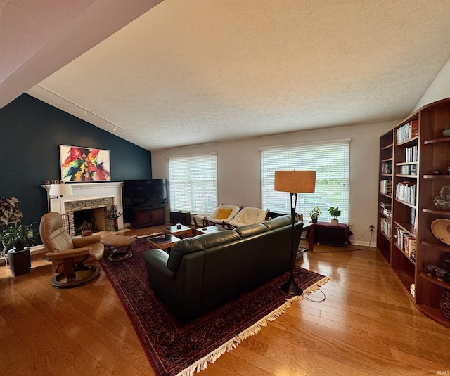 living area with wood finished floors, lofted ceiling, a fireplace, a textured ceiling, and baseboards