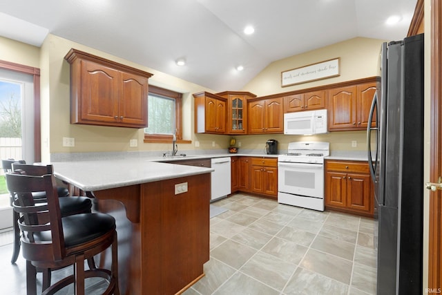 kitchen featuring white appliances, a peninsula, lofted ceiling, a sink, and brown cabinetry