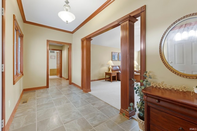 hall featuring decorative columns, crown molding, baseboards, and light carpet
