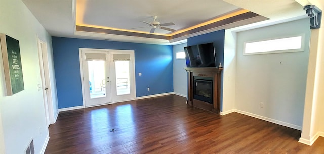 unfurnished living room with a raised ceiling, a ceiling fan, a glass covered fireplace, and wood finished floors