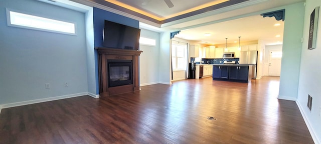 unfurnished living room with a glass covered fireplace, dark wood finished floors, ceiling fan, baseboards, and crown molding