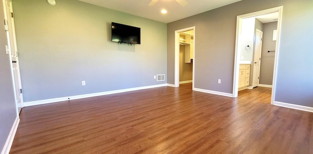 unfurnished bedroom featuring dark wood-style floors, a walk in closet, baseboards, a ceiling fan, and a closet