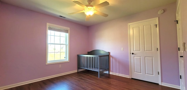 unfurnished bedroom with dark wood-style floors, baseboards, a ceiling fan, and a crib