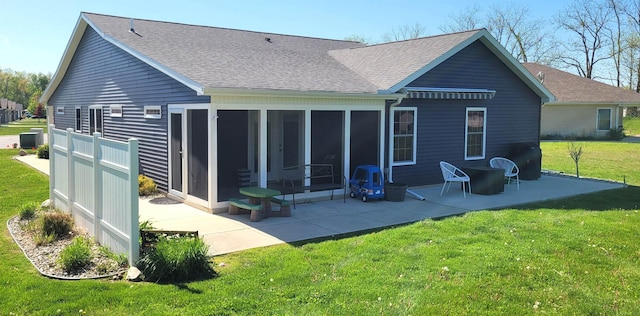 rear view of property featuring roof with shingles, a patio, a sunroom, and a lawn
