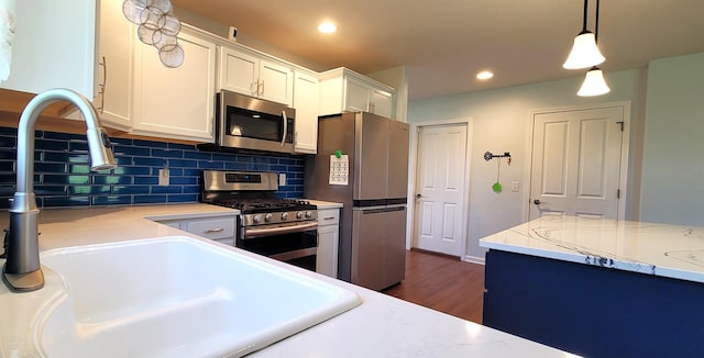 kitchen featuring stainless steel appliances, a sink, white cabinets, decorative backsplash, and pendant lighting