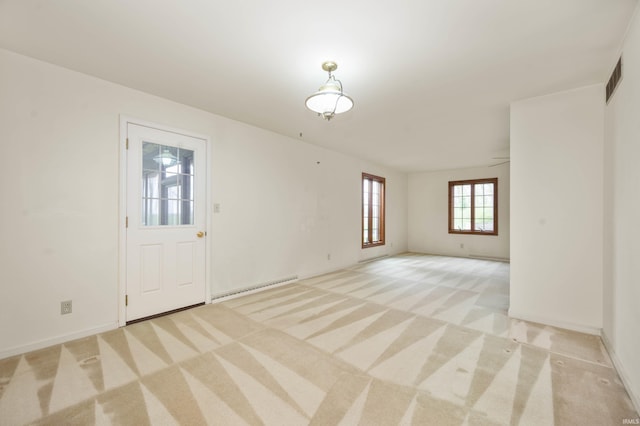 spare room with a baseboard heating unit, light carpet, and baseboards