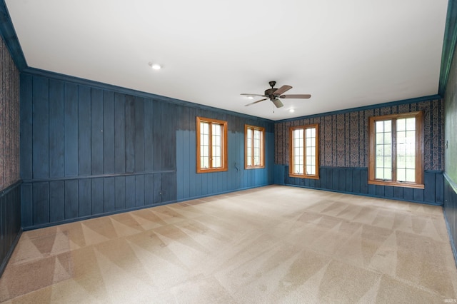 carpeted empty room featuring ceiling fan, healthy amount of natural light, wood walls, wainscoting, and ornamental molding