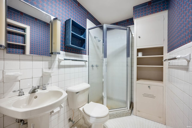 full bath featuring tile walls, wallpapered walls, a shower stall, a sink, and toilet