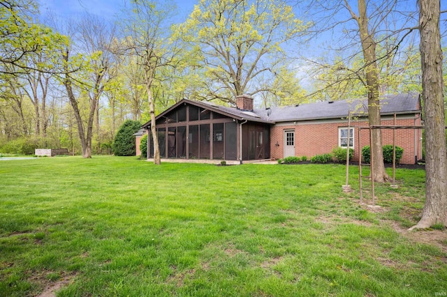 rear view of property featuring a sunroom, a chimney, a lawn, and brick siding