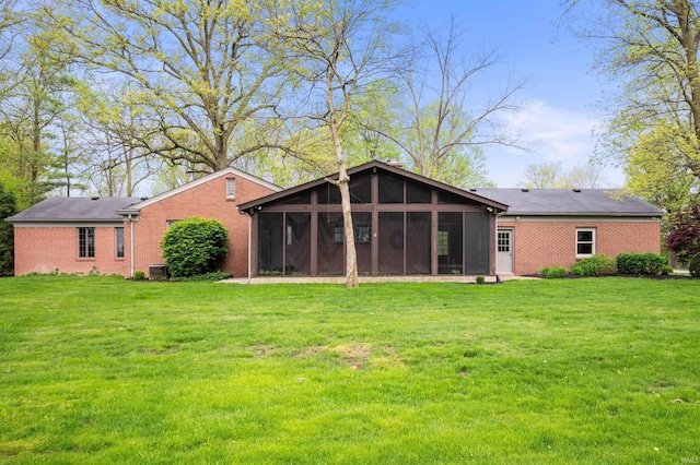 back of house featuring a sunroom, brick siding, and a lawn
