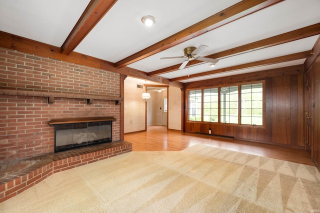 unfurnished living room featuring carpet flooring, a fireplace, a ceiling fan, wood finished floors, and beamed ceiling