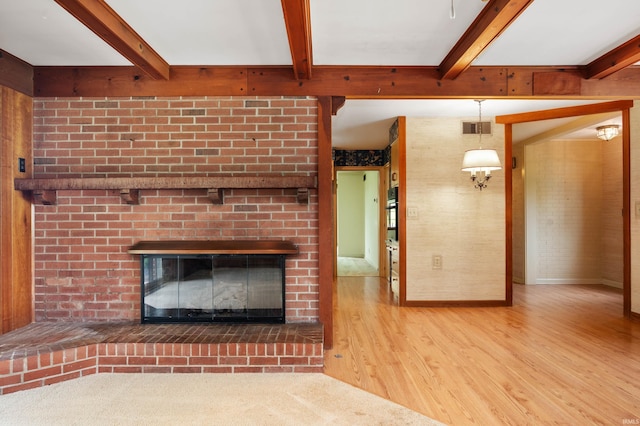 unfurnished living room featuring wood finished floors, beamed ceiling, and a brick fireplace