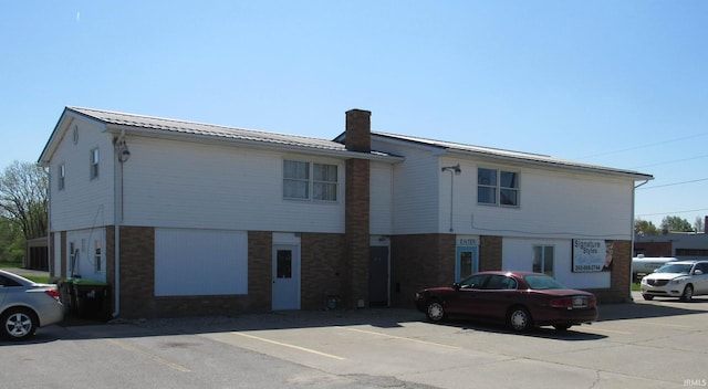 rear view of house with uncovered parking, brick siding, a chimney, and metal roof