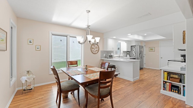 dining space with light wood finished floors, a chandelier, baseboards, a raised ceiling, and recessed lighting