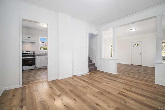 unfurnished living room with stairway, ornate columns, light wood-style flooring, ornamental molding, and baseboards