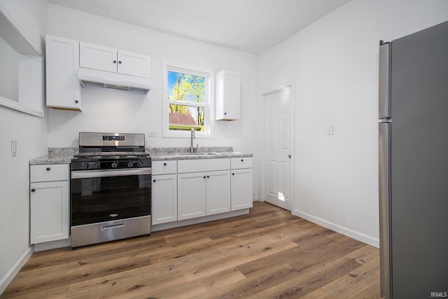 kitchen with stainless steel appliances, under cabinet range hood, light wood-type flooring, white cabinetry, and a sink