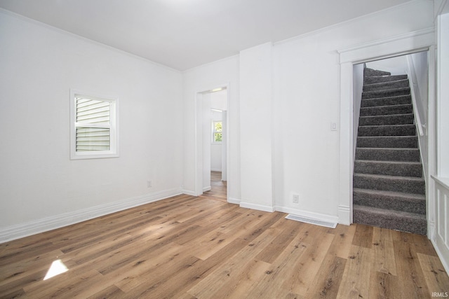 spare room with plenty of natural light, stairs, light wood-style flooring, baseboards, and crown molding