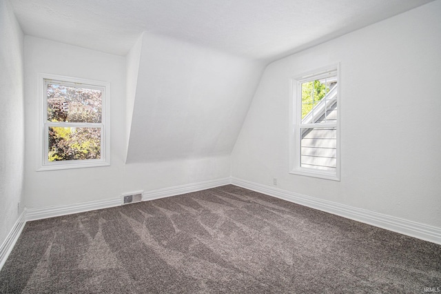 additional living space with dark colored carpet, vaulted ceiling, and baseboards