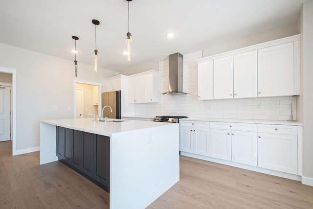 kitchen featuring wall chimney range hood, decorative backsplash, light wood-style flooring, white cabinetry, and a sink