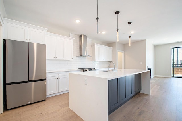 kitchen featuring freestanding refrigerator, wall chimney exhaust hood, a sink, white cabinetry, and recessed lighting