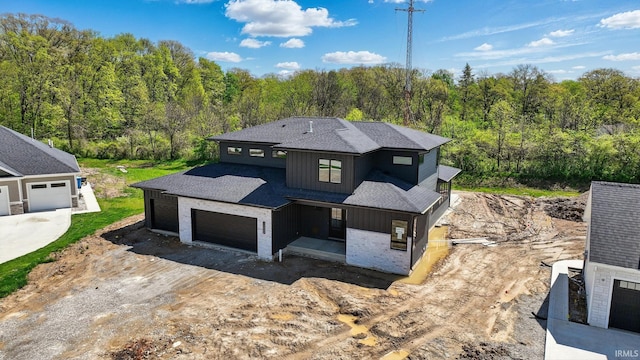 13222 Malfini Trl, Fort Wayne, IN 46845 - view of front facade with board and batten siding, a garage, a wooded view, roof with shingles, and dirt driveway