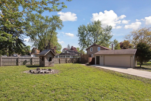 view of yard with concrete driveway, an attached garage, a fire pit, an outbuilding, and a shed