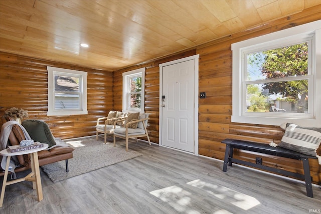 sitting room with log walls, wooden ceiling, healthy amount of natural light, and wood finished floors