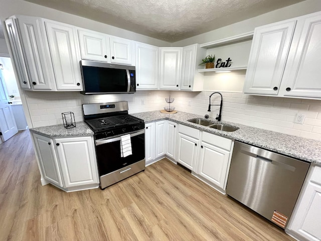 kitchen featuring stainless steel appliances, a sink, white cabinetry, a textured ceiling, and open shelves