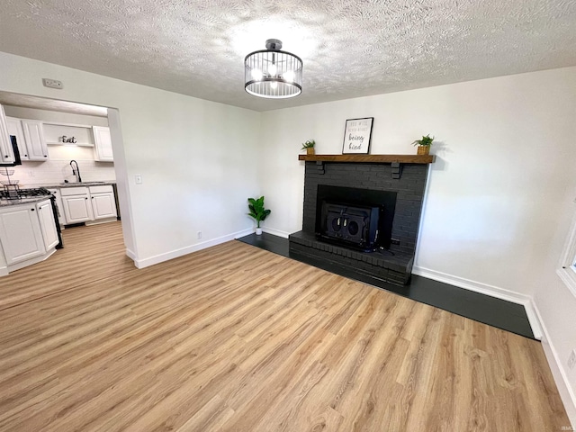 unfurnished living room featuring baseboards, a textured ceiling, light wood finished floors, a fireplace, and a sink