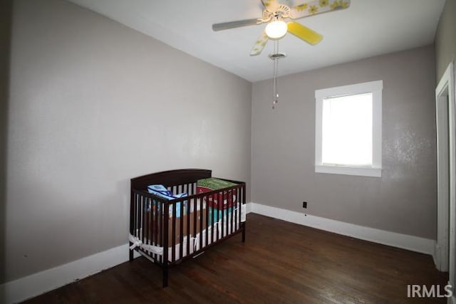 128 E Washington St, Williamsport, IN 47993 - bedroom with baseboards, wood finished floors, a crib, and a ceiling fan