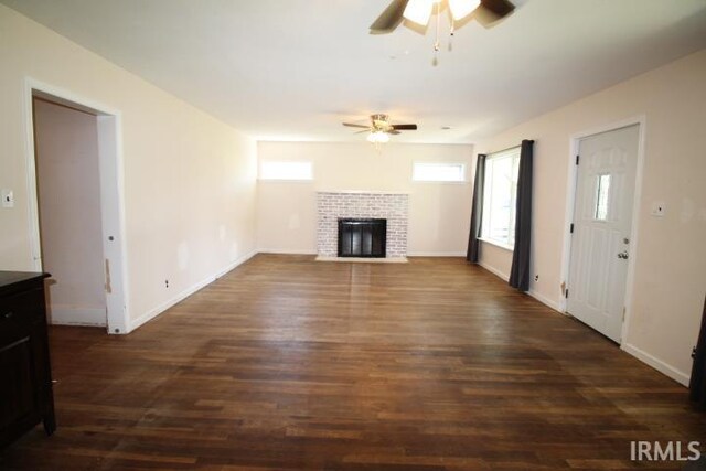 128 E Washington St, Williamsport, IN 47993 - unfurnished living room with ceiling fan, dark wood finished floors, a tiled fireplace, and baseboards