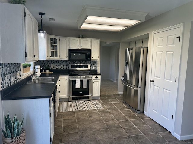 kitchen featuring stainless steel appliances, dark countertops, a sink, decorative backsplash, and white cabinets