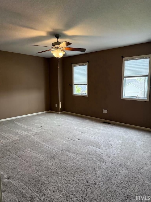 carpeted spare room with a ceiling fan and baseboards