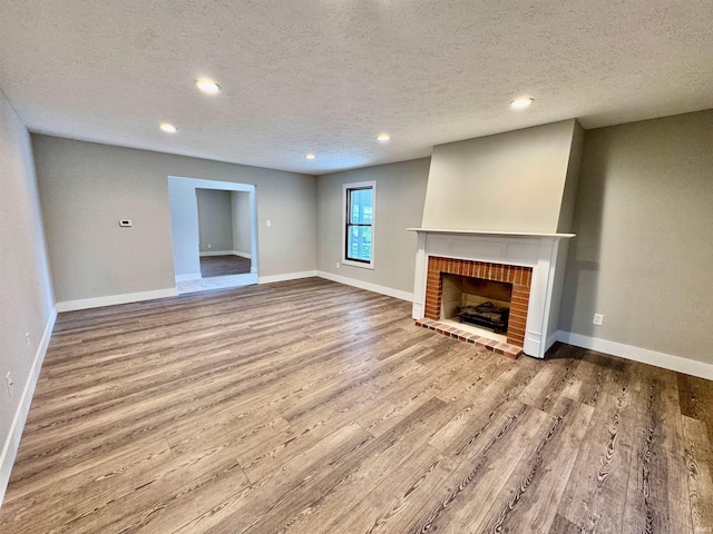 unfurnished living room featuring wood finished floors, recessed lighting, a brick fireplace, a textured ceiling, and baseboards