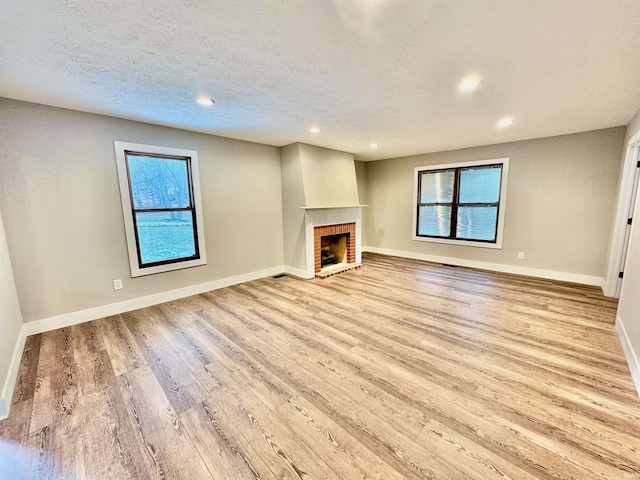 unfurnished living room with a fireplace, light wood-type flooring, plenty of natural light, baseboards, and recessed lighting