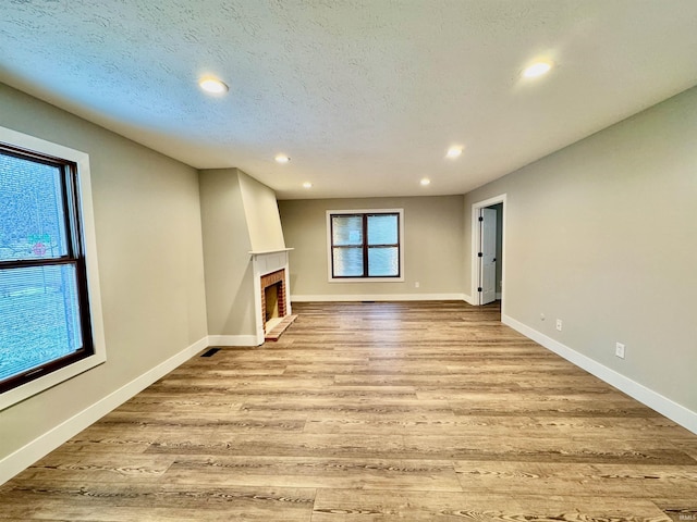 unfurnished living room with a fireplace, recessed lighting, light wood finished floors, baseboards, and a textured ceiling