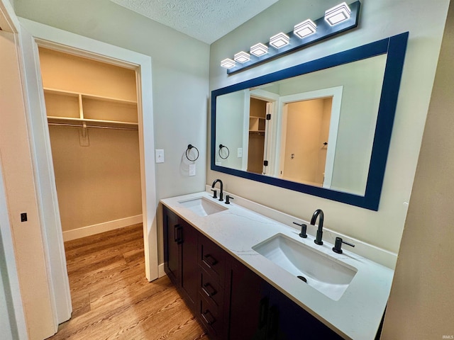 full bath with wood finished floors, a textured ceiling, double vanity, and a walk in closet