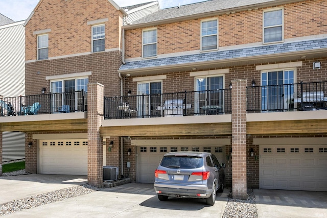 rear view of property with brick siding, a garage, driveway, and cooling unit