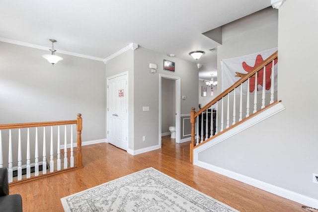 foyer with wood finished floors, ornamental molding, baseboards, a chandelier, and stairway