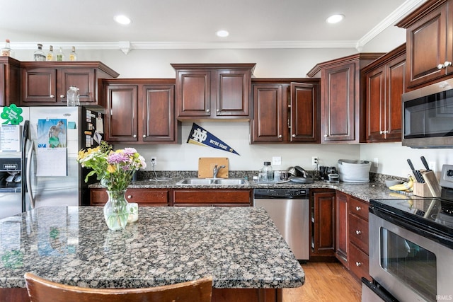 kitchen with appliances with stainless steel finishes, a sink, dark stone counters, crown molding, and light wood finished floors