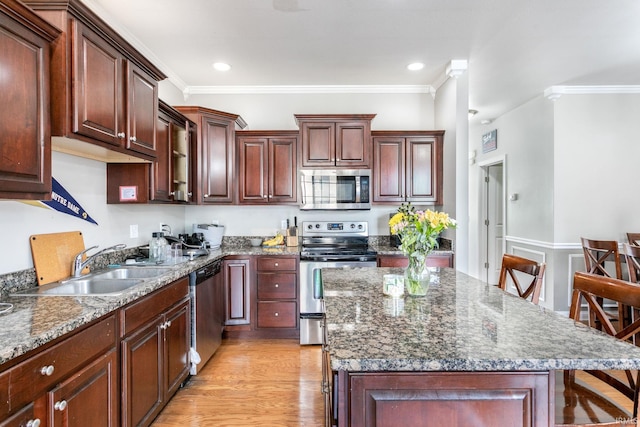kitchen with appliances with stainless steel finishes, a kitchen island, crown molding, light wood-style flooring, and a sink