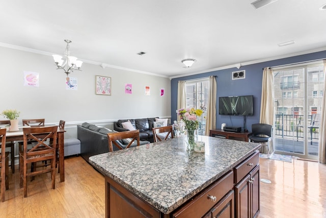 kitchen featuring light wood finished floors, ornamental molding, a chandelier, open floor plan, and stone counters