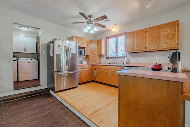 kitchen featuring stainless steel appliances, washer and dryer, wood finished floors, a sink, and a peninsula