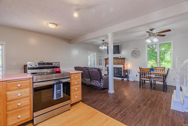 kitchen featuring stainless steel range with electric stovetop, ceiling fan, wood finished floors, light countertops, and a glass covered fireplace