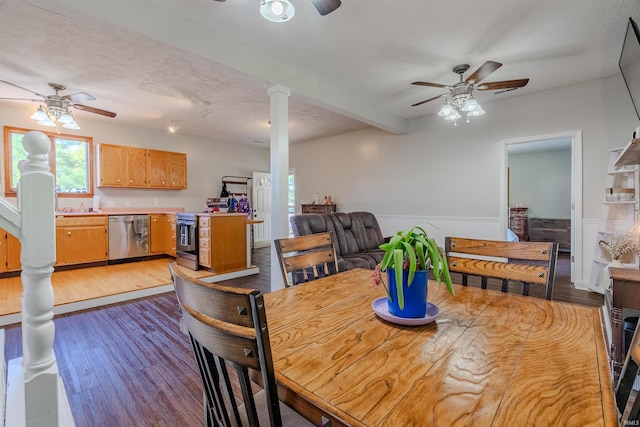 dining space with a ceiling fan, ornate columns, wood finished floors, wainscoting, and a textured ceiling