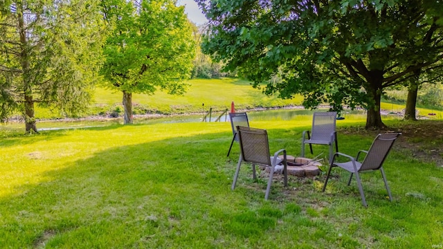 view of green lawn featuring a water view and a fire pit